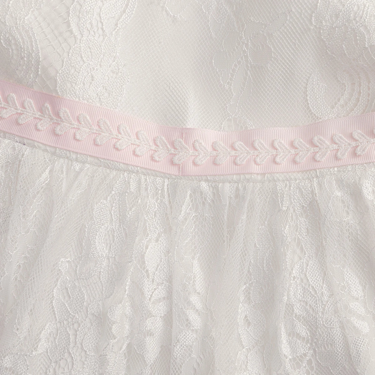 Tabitha Elegant Baptism Flower Girl Dress against white lace fabric with a pink waist ribbon.