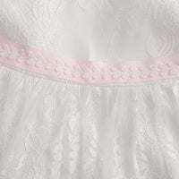 Tabitha Elegant Baptism Flower Girl Dress against white lace fabric with a pink waist ribbon.