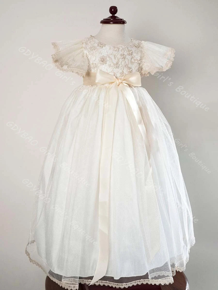 White baby girl christening gown with beaded lace bodice, flutter sleeves, satin bow sash, and tulle skirt.