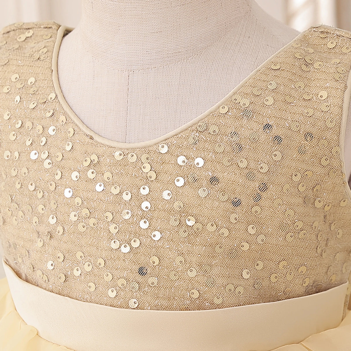 A sleeveless beige blouse with dense silver sequin embellishments across the bodice, displayed on a cream-colored dress form mannequin.