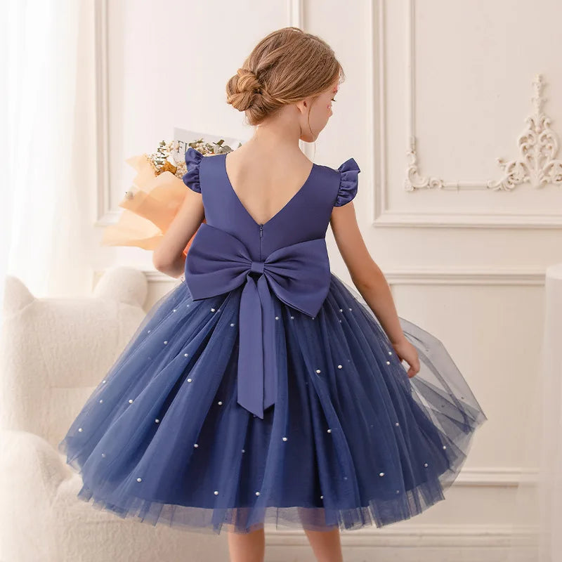 A back view of a girl in a navy blue 'Chantelle-Elise' V-Back Occasion Dress, featuring a beautiful bow and flowing skirt, ideal for formal events.