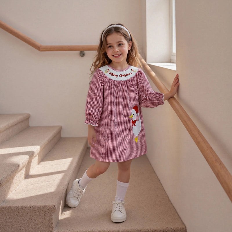 Merry Christmas, Ducky! Checked Smocked Dress on a young girl standing on stairs, featuring an embroidered Santa Duck and whimsical red and white checked fabric.