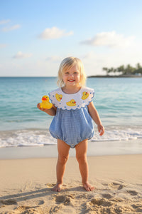 Blue checkered baby romper with duck design on a hanger against a white wall.