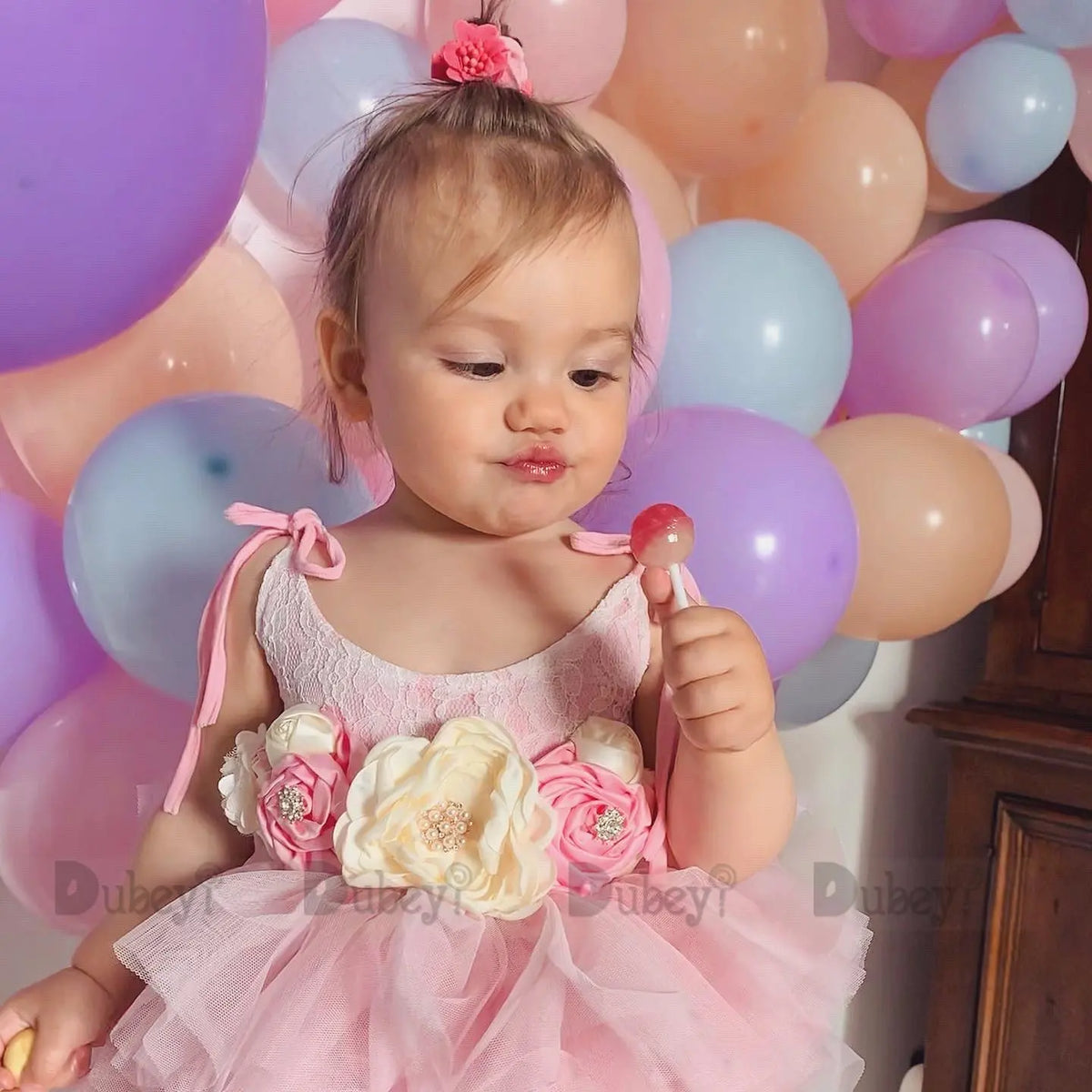 Toddler girl in Cecilia vintage tiered tulle dress with belt and headband among pastel balloons.
