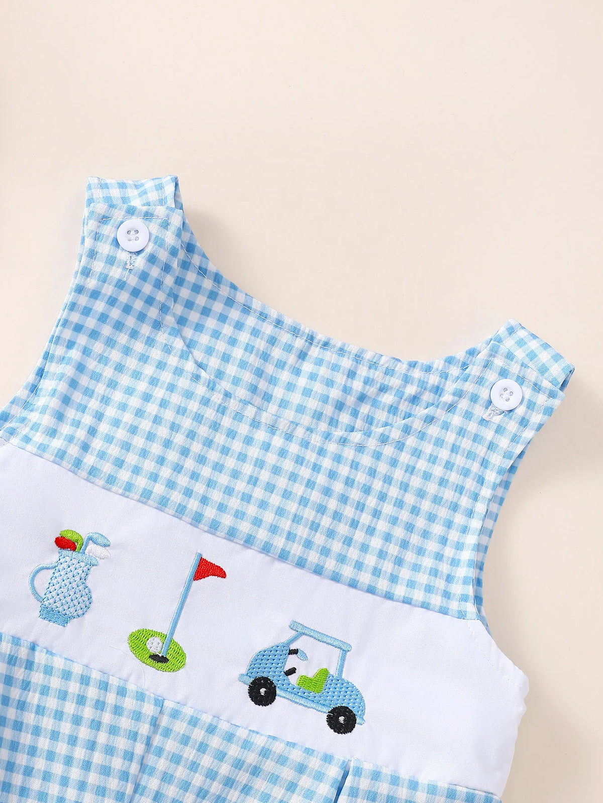 Blue and white gingham sleeveless baby romper with embroidered golf cart, flag, and bag on white panel with button shoulder closures.