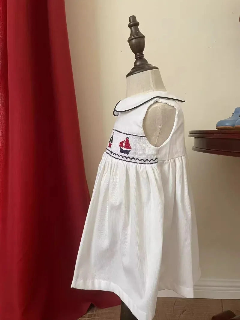 Little girl wearing the Set Sail Party Dress in a garden setting, highlighting the classic nautical theme and knee-length skirt.