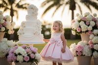 Pink dress on a mannequin with a decorative bow, set against a blurred indoor background.