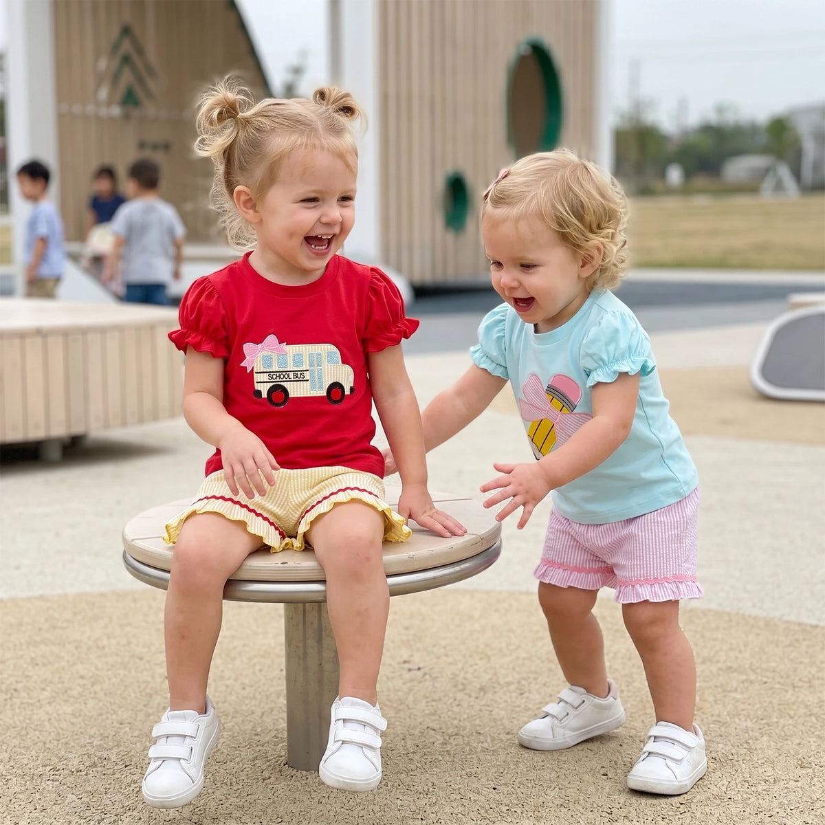 Two toddlers in puff-sleeve tees and striped shorts with embroidered bus and heart designs, frilly accents.