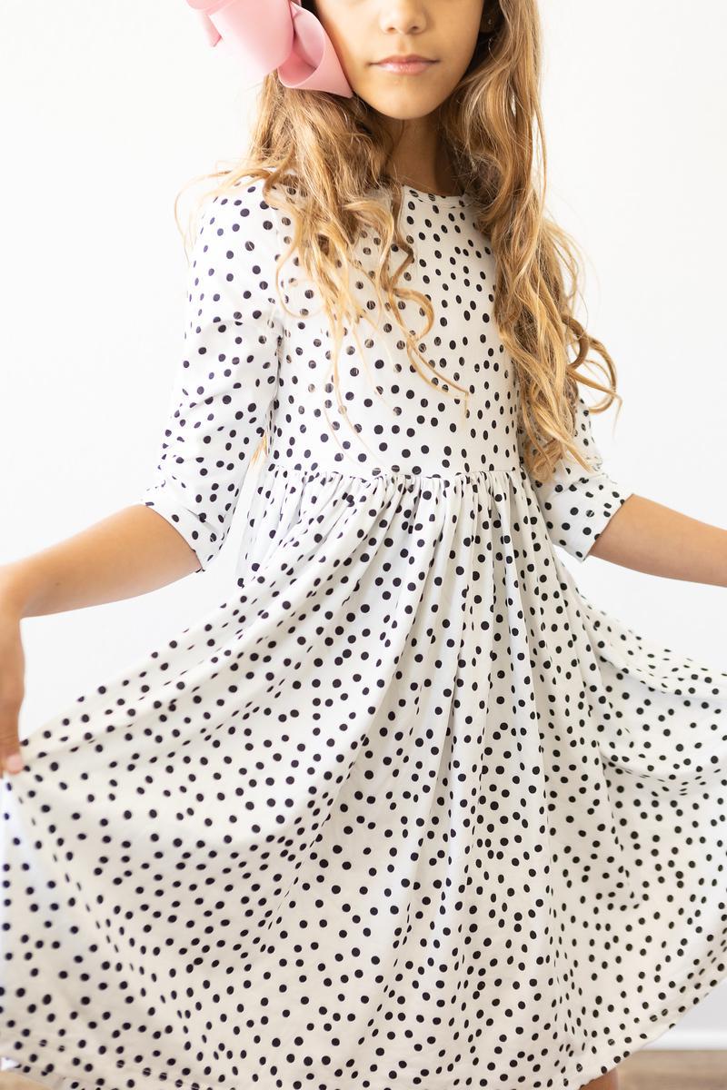 Little girl twirling in a Scattered Dot 3/4 Sleeve Pocket Twirl Dress, showcasing a playful black polka dot print on a white background.