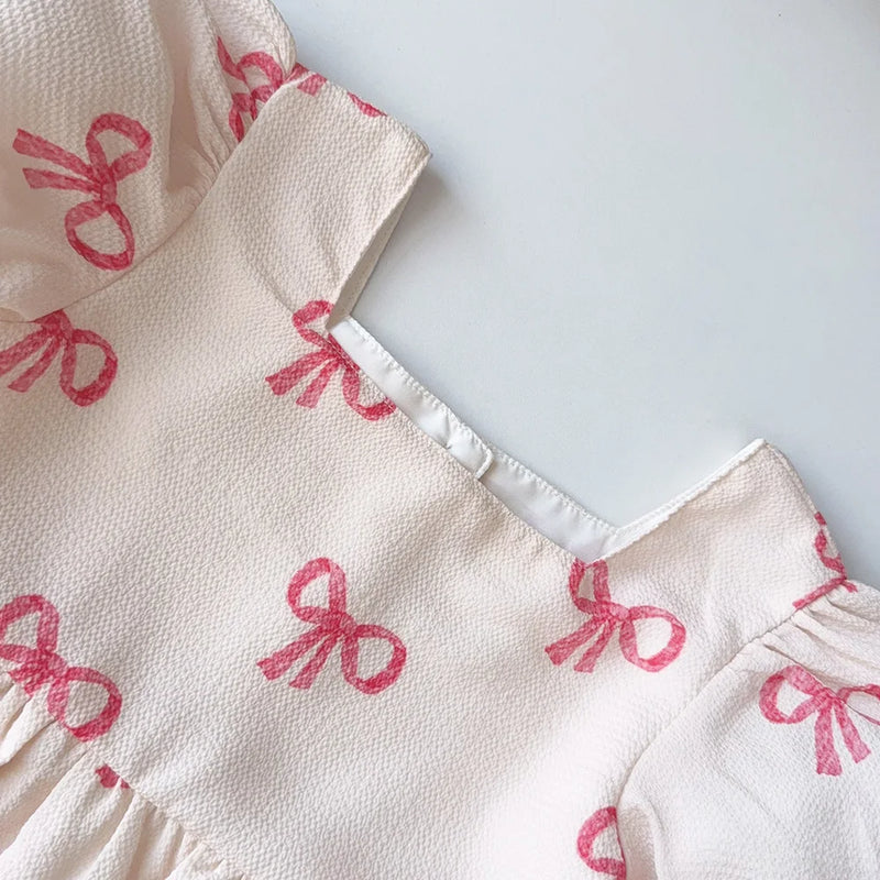 Close-up of the square neckline and puff sleeves of the Sweet Little Bows Party Dress, showcasing the adorable pink bow design.