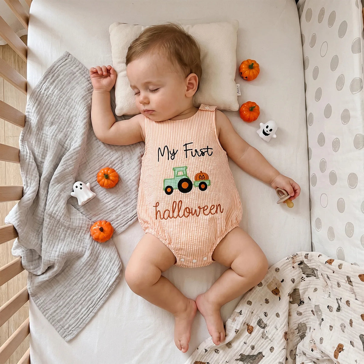 Sleeping baby in orange and white seersucker bubble with pumpkin truck applique and My First Halloween text.