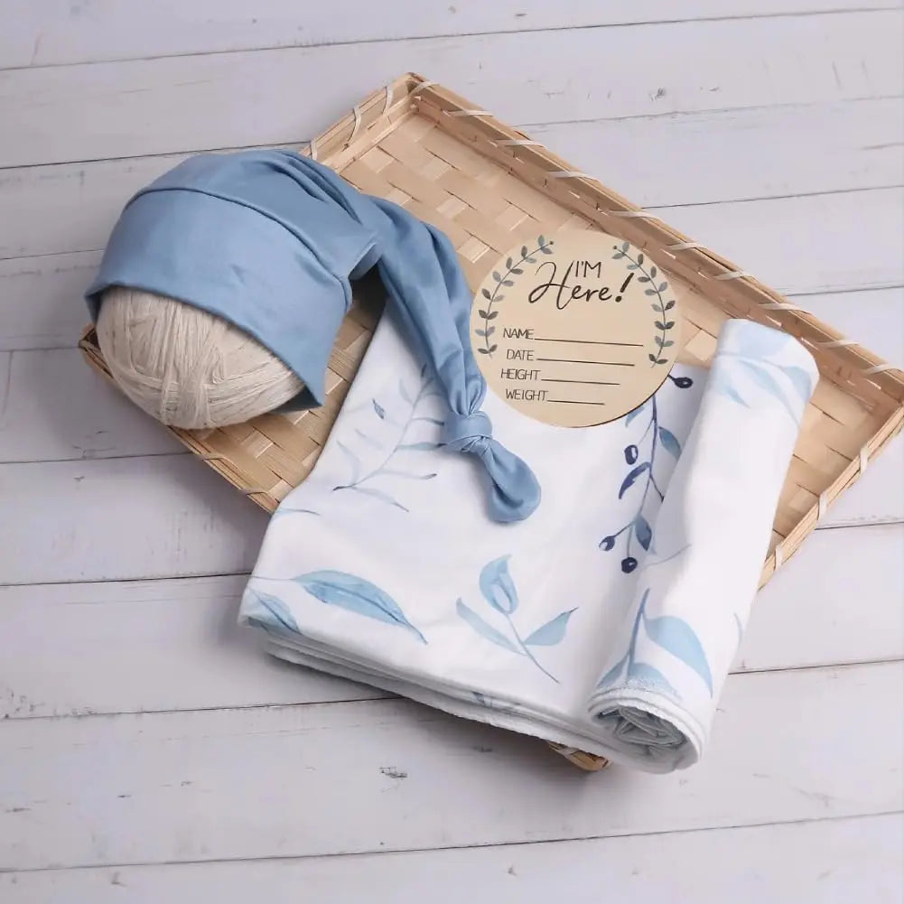 Blue leaf print baby swaddle blanket and matching long tie hat in a tray with an I'm Here tag.