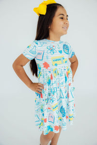 Girl in School Rules Short Sleeve Pocket Twirl Dress with a yellow hair bow, smiling.