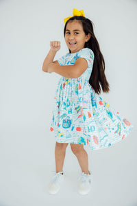 Girl wearing a light-blue School Rules Short Sleeve Pocket Twirl Dress with a bright yellow bow.