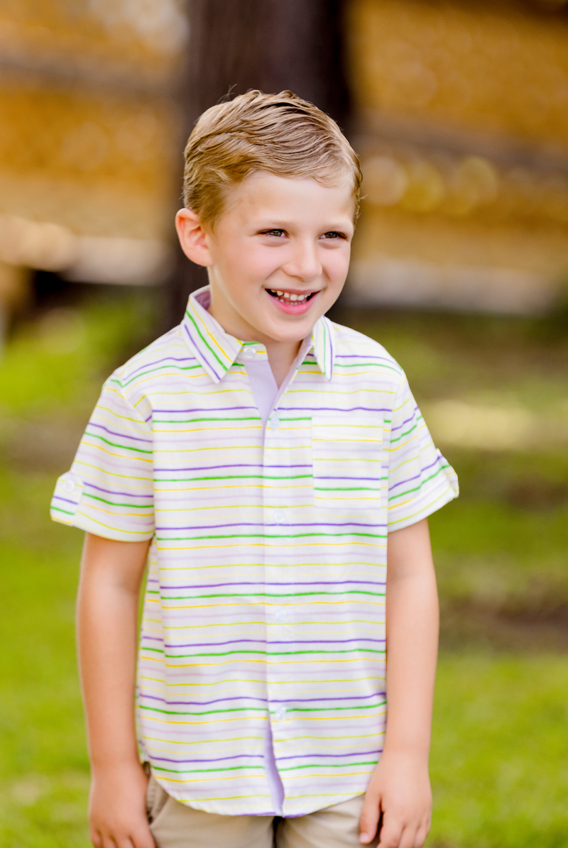Boy wearing Carnival Time striped short-sleeve collared shirt with purple, green, and gold stripes outdoors.