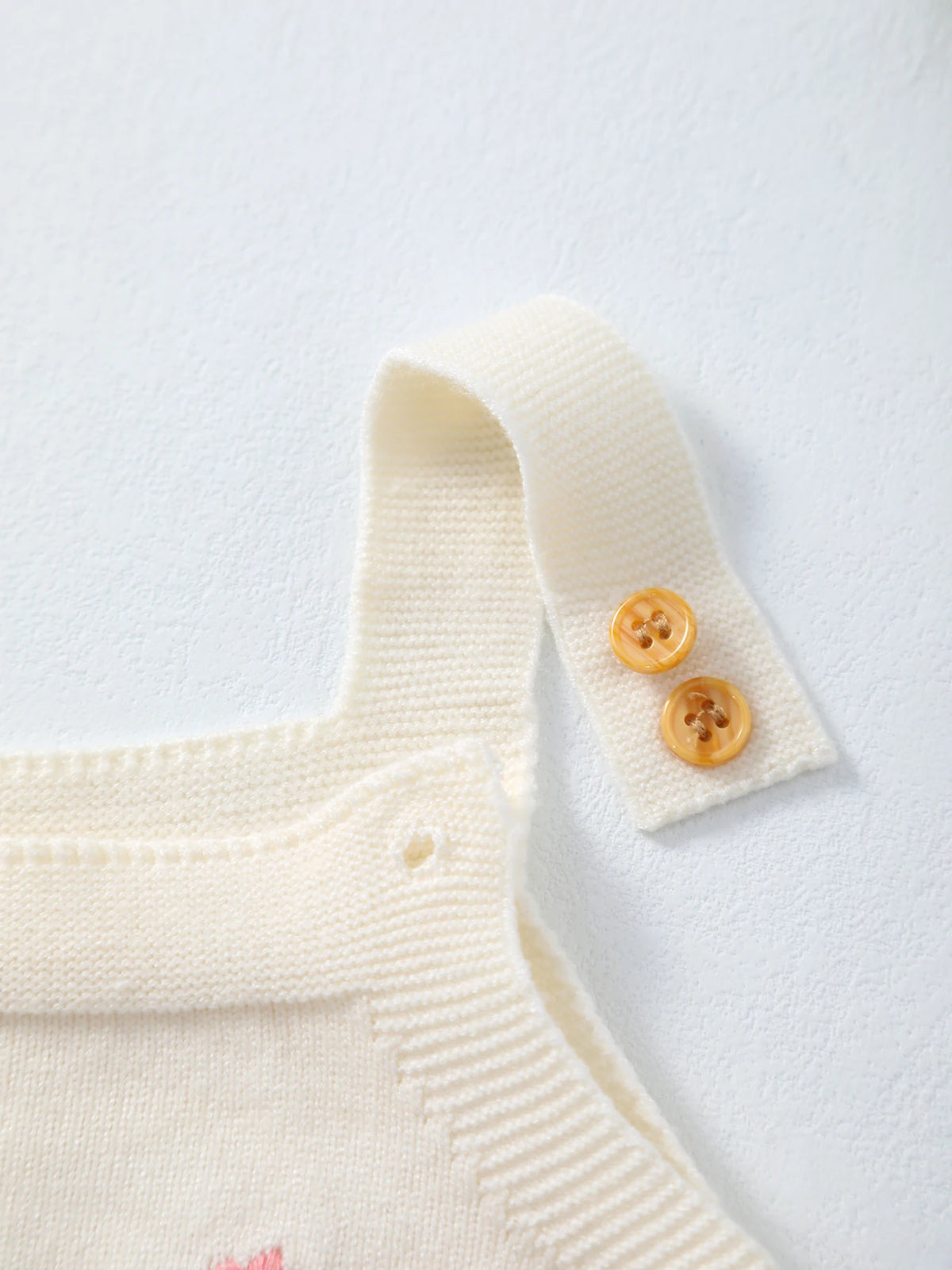 Cream knit romper strap with two amber buttons for babies.