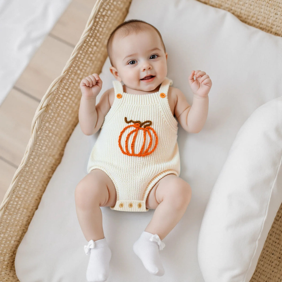 Smiling baby wears cream knit romper overalls with orange embroidered pumpkin. Sleeveless, breathable outfit for toddlers.