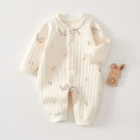 Cream quilted baby romper with long sleeves, featuring printed prams, rabbits, and rainbows, displayed flat beside a wooden bunny teether.