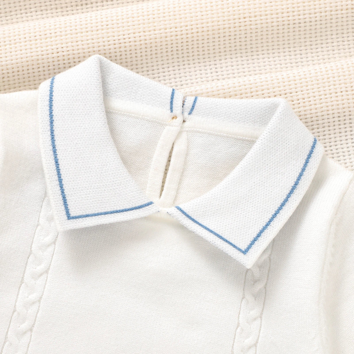 Close-up of a white knit collar with light blue piping, shown on a cream textured fabric background.