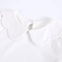 Close-up of a white baby or toddler top featuring a large, soft scalloped Peter Pan collar and a small front tie detail.