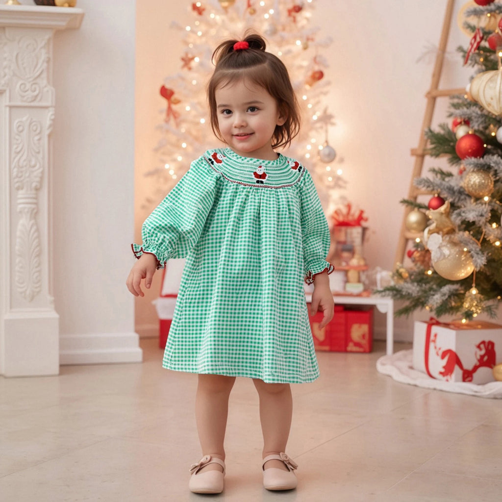 Toddler wearing the Adorable Santa Rudy Reindeer Smocked Dress in Wreath green checks, smiling in front of a beautifully decorated Christmas tree.