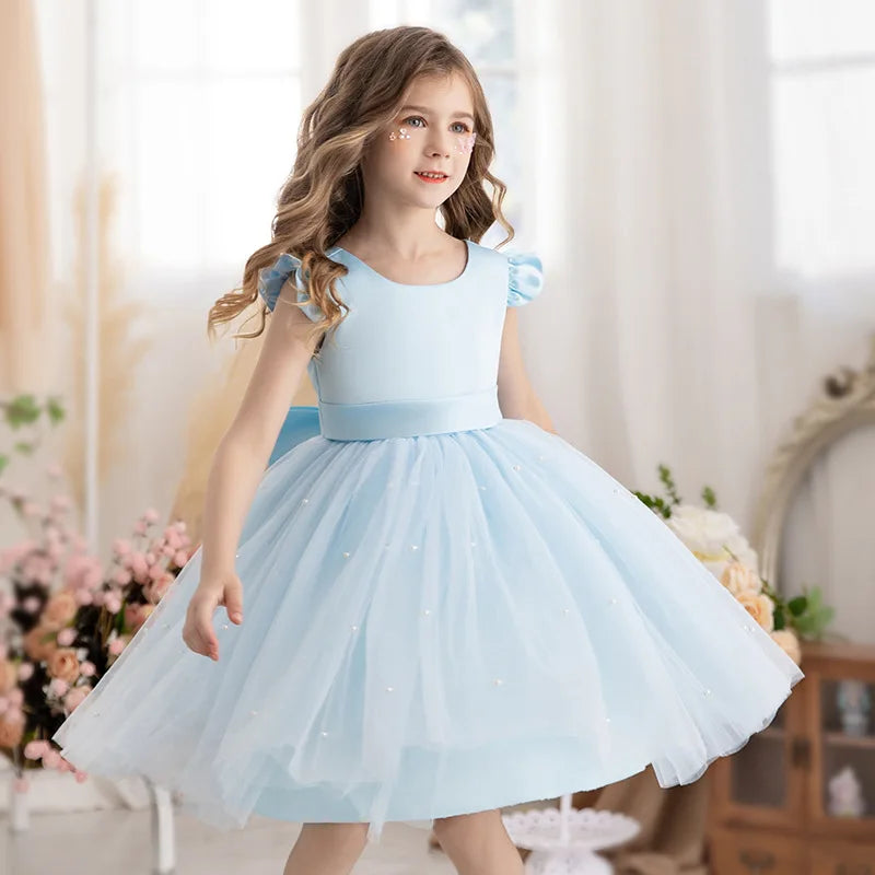 A girl in a soft blue 'Chantelle-Elise' V-Back Occasion Dress, twirling in her elegant tulle skirt, ideal for any celebratory event.