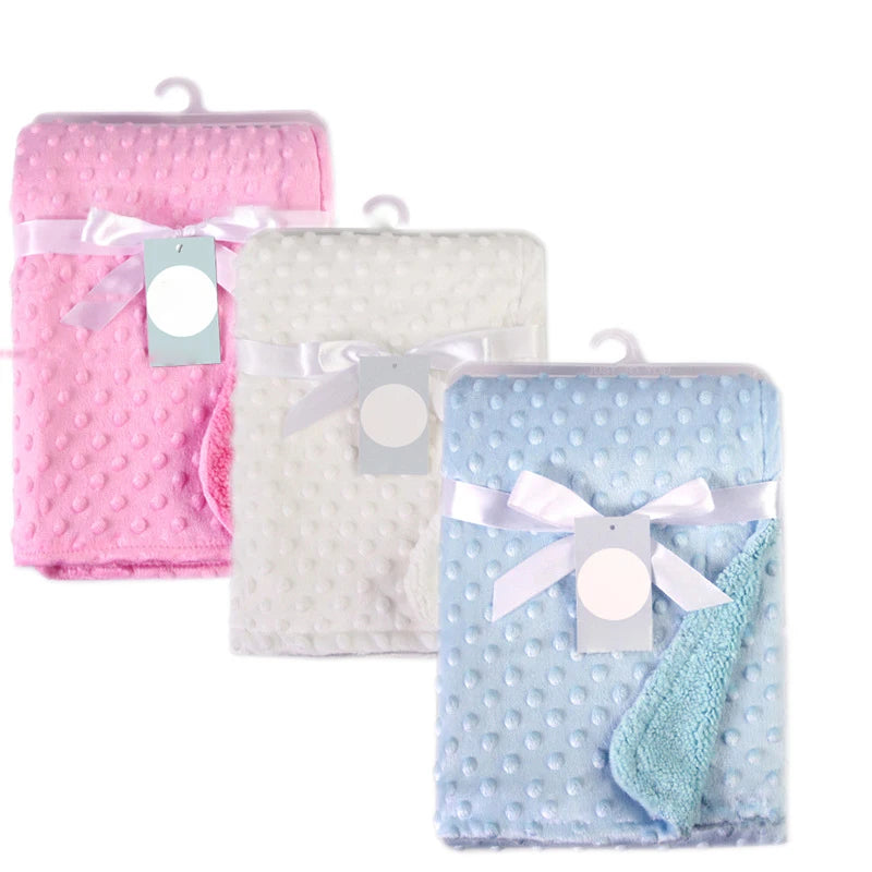 Set of three dotted soft fleece baby blankets in pink, white, and blue with ribbons and tags.