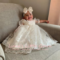 Mila Heirloom Lace Baptism Gown on a smiling baby girl with lace overlay, embroidered flowers, and bow.