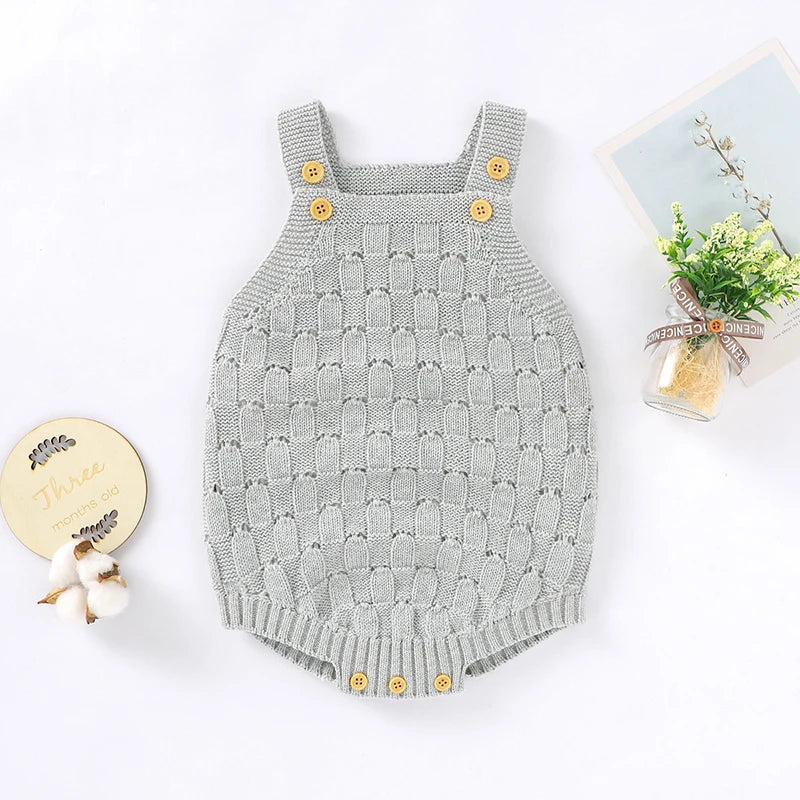 A light gray knit baby romper with yellow buttons, styled in a flat-lay arrangement with decorative props on a white background.