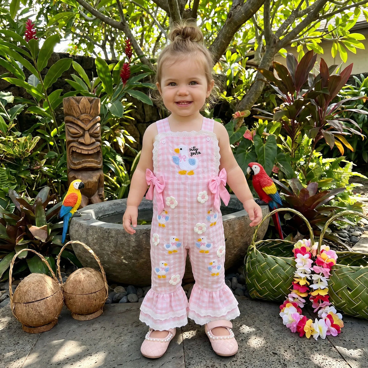 Young girl in a pink floral dress standing outdoors with plants and a tiki statue in the background.