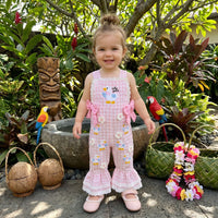 Young girl in a pink floral dress standing outdoors with plants and a tiki statue in the background.