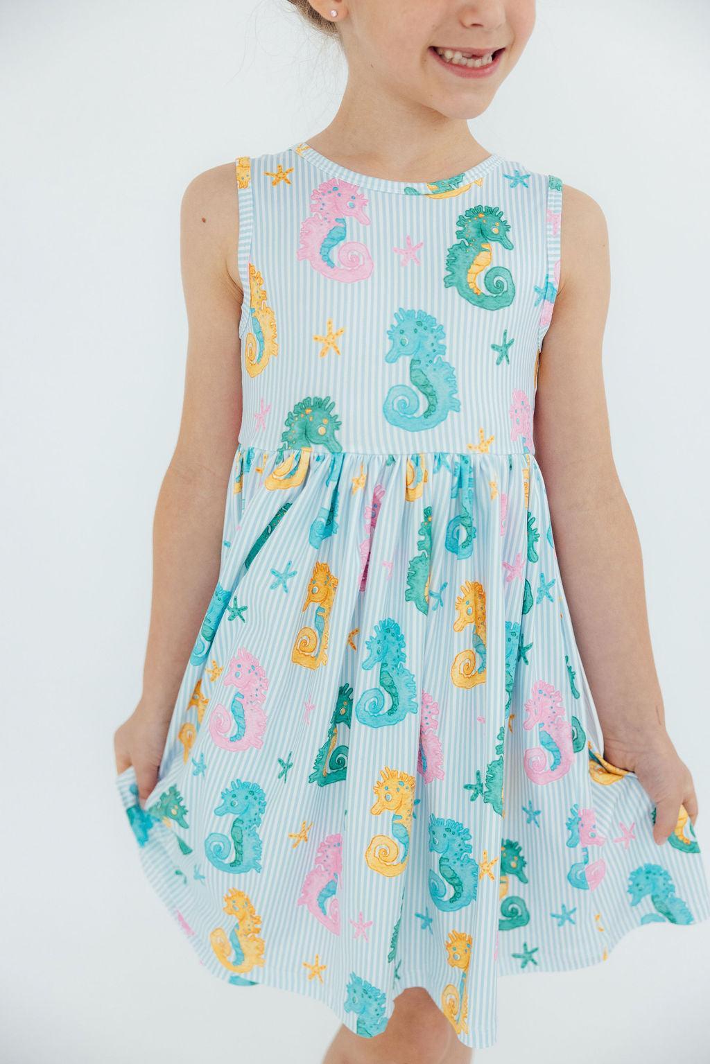 Little girl wearing the Seahorse Swirl Tank Twirl Dress for girls, twirling joyfully in a sunny playground.