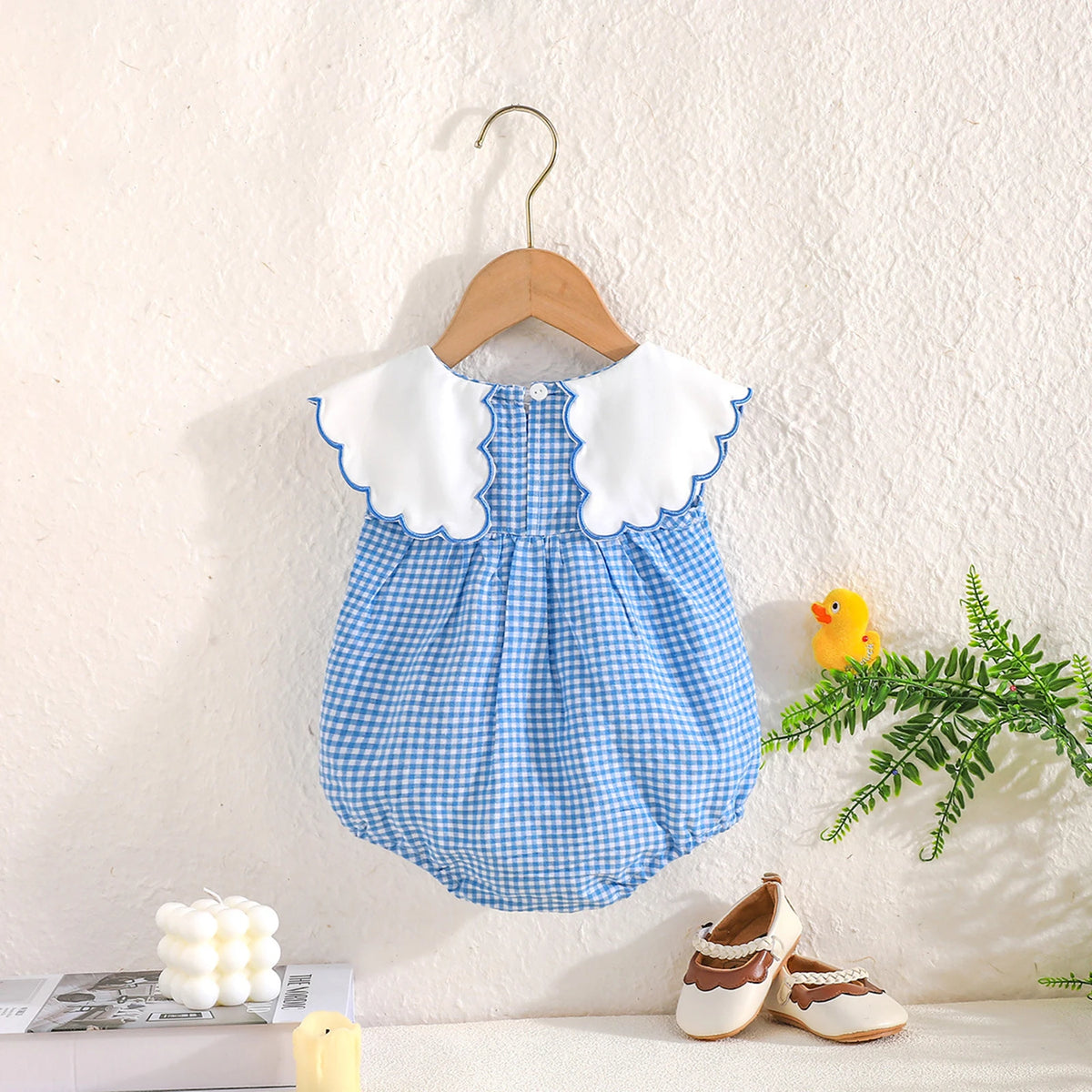 Plaid blue gingham baby bubble romper with a white scalloped embroidered Peter Pan collar on a hanger.