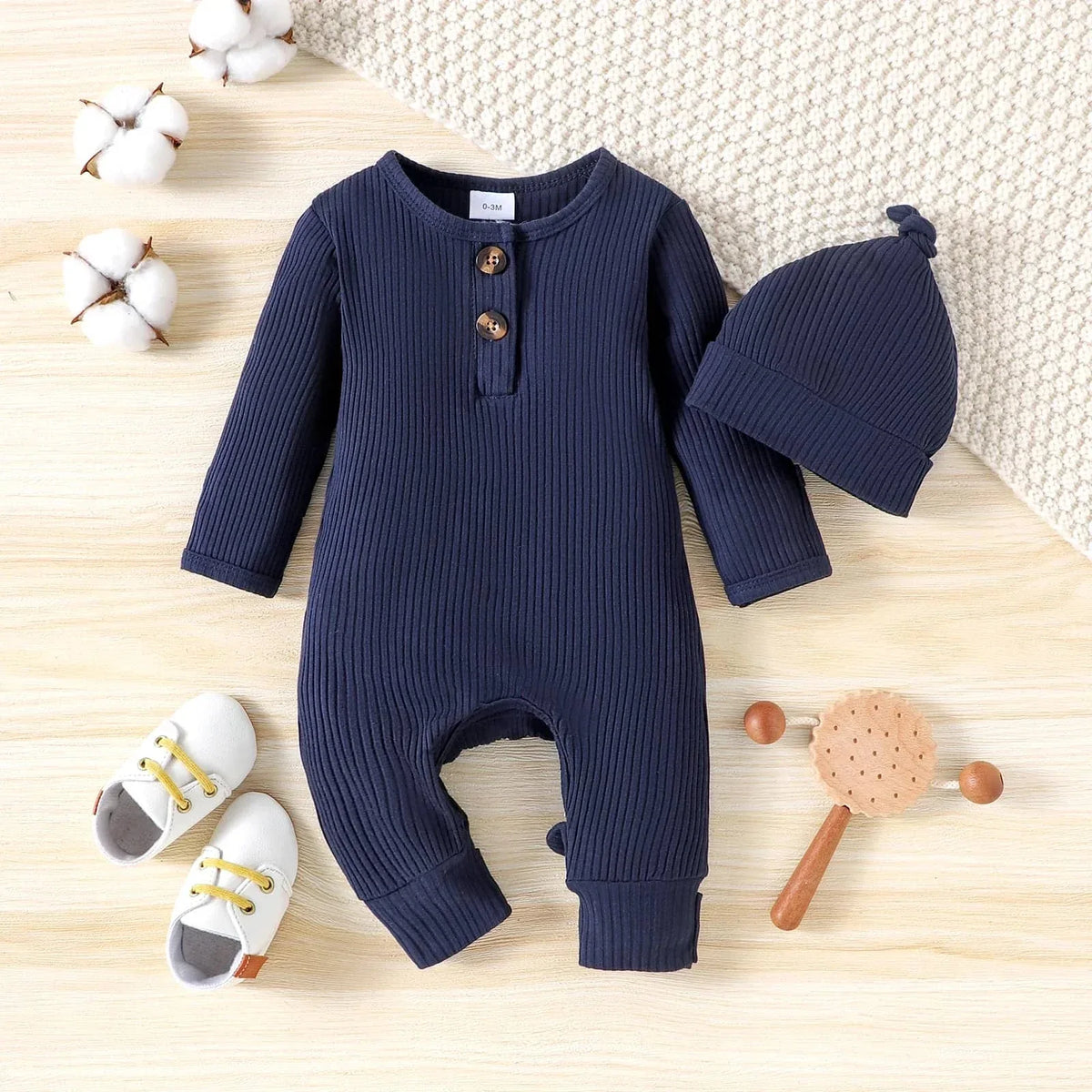 Navy blue ribbed romper for babies with matching hat and white baby shoes on wooden surface