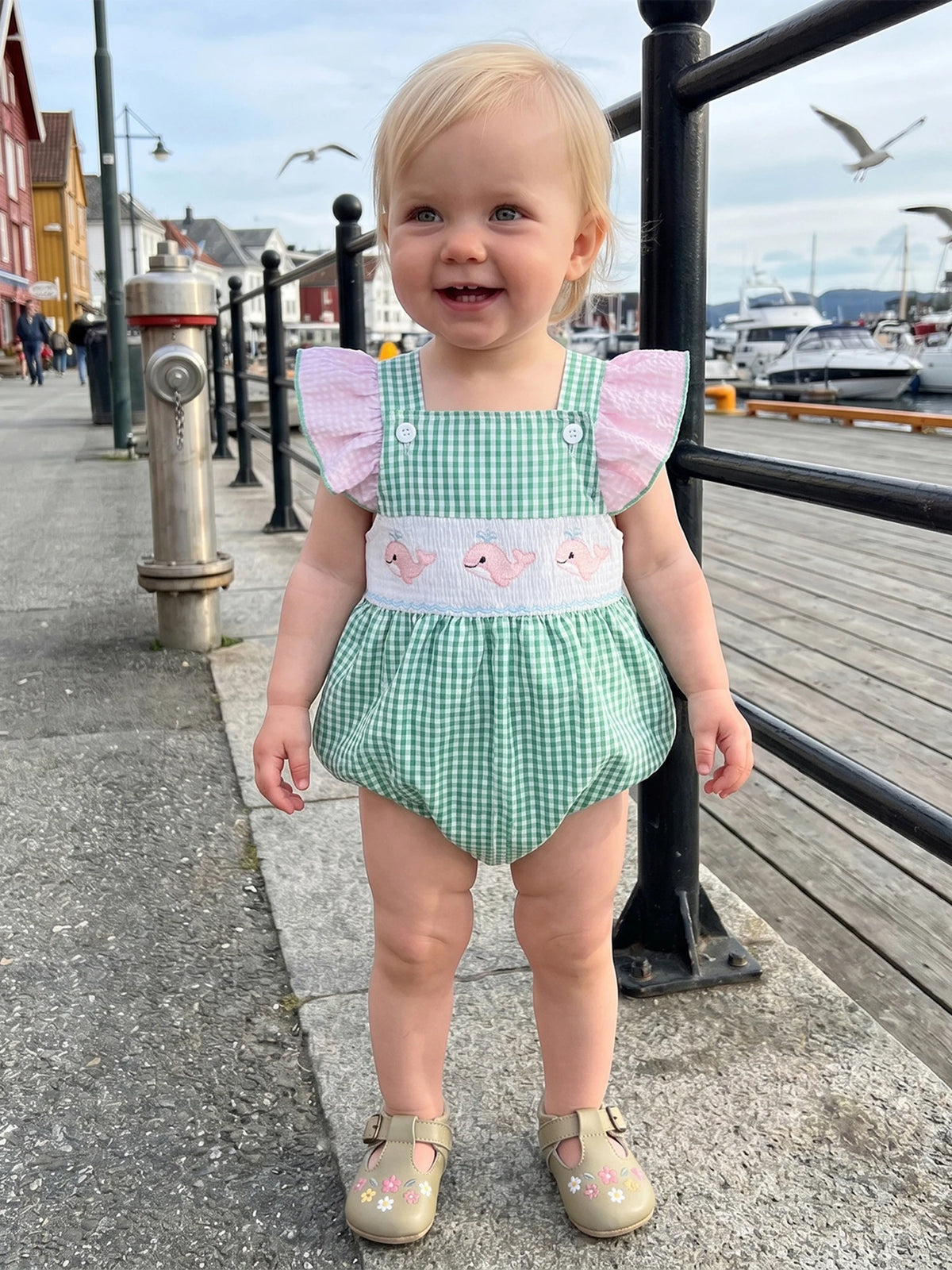 Toddler in Take Me Out To The Seashore Romper: green gingham, pink flutter sleeves, sea-creature embroidery by harbor.