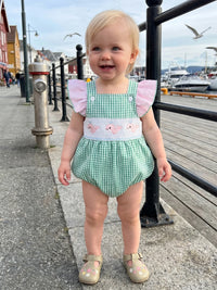 Toddler in Take Me Out To The Seashore Romper: green gingham, pink flutter sleeves, sea-creature embroidery by harbor.