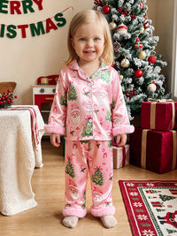 Pink satin Christmas pajama set for girls featuring Santa, trees, and bows with fuzzy cuff accents. Perfect holiday loungewear.