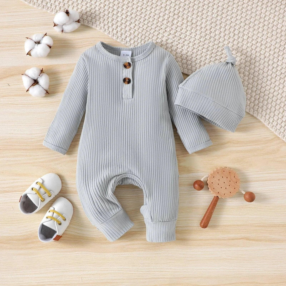 light gray ribbed romper for babies with matching knot hat laid flat with baby shoes and wooden rattle