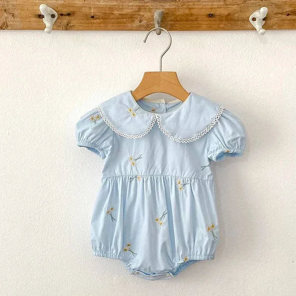Light blue embroidered baby bubble romper with puff sleeves and white lace collar hanging on wooden hanger