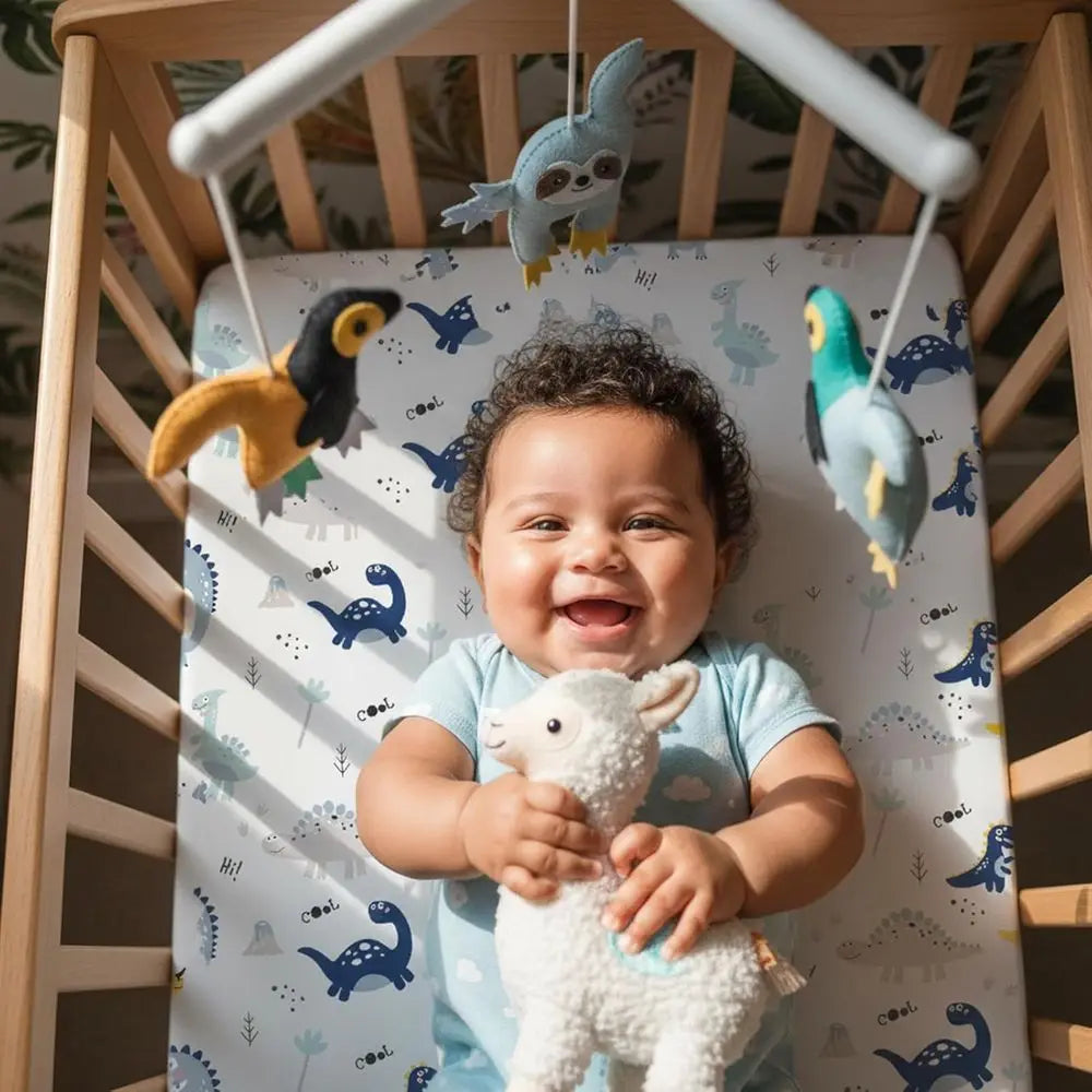 Smiling baby in crib on dinosaur-print microfiber crib sheet (52x28), 4-pack, 100% polyester, US origin.