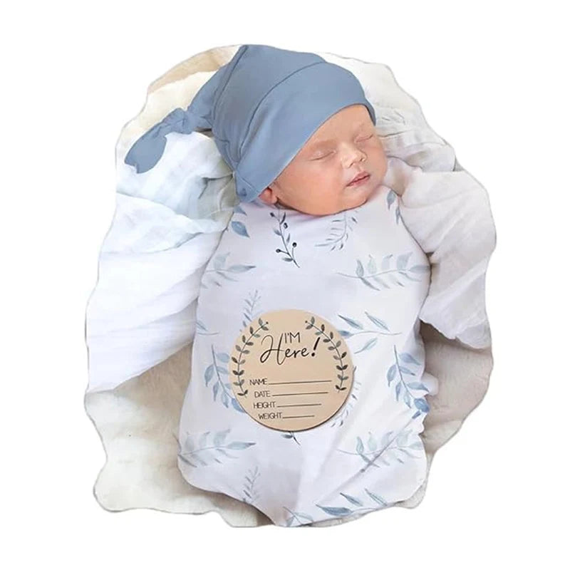 Soft white swaddle blanket with blue leaf print and matching blue knit cap. Features "I'm Here" info patch. Perfect baby shower gift set.