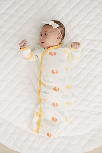Baby wearing GOTS certified organic cotton sleep gown with smiley bolt pattern and yellow trim on white quilted mat.