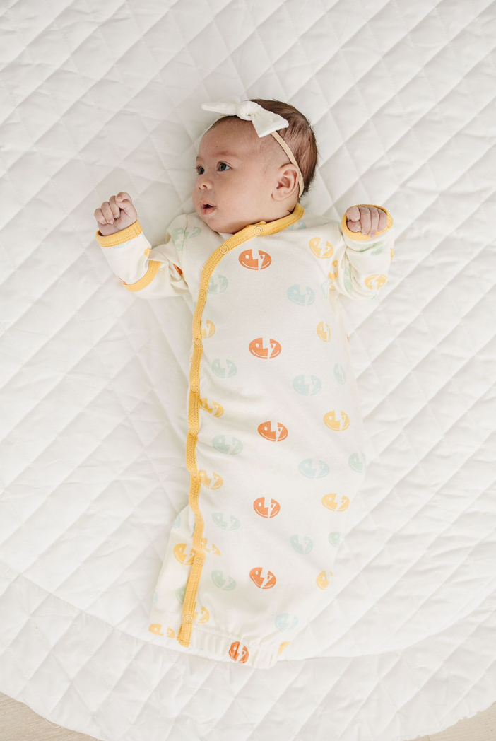 Baby wearing GOTS certified organic cotton sleep gown with smiley bolt pattern and yellow trim on white quilted mat.
