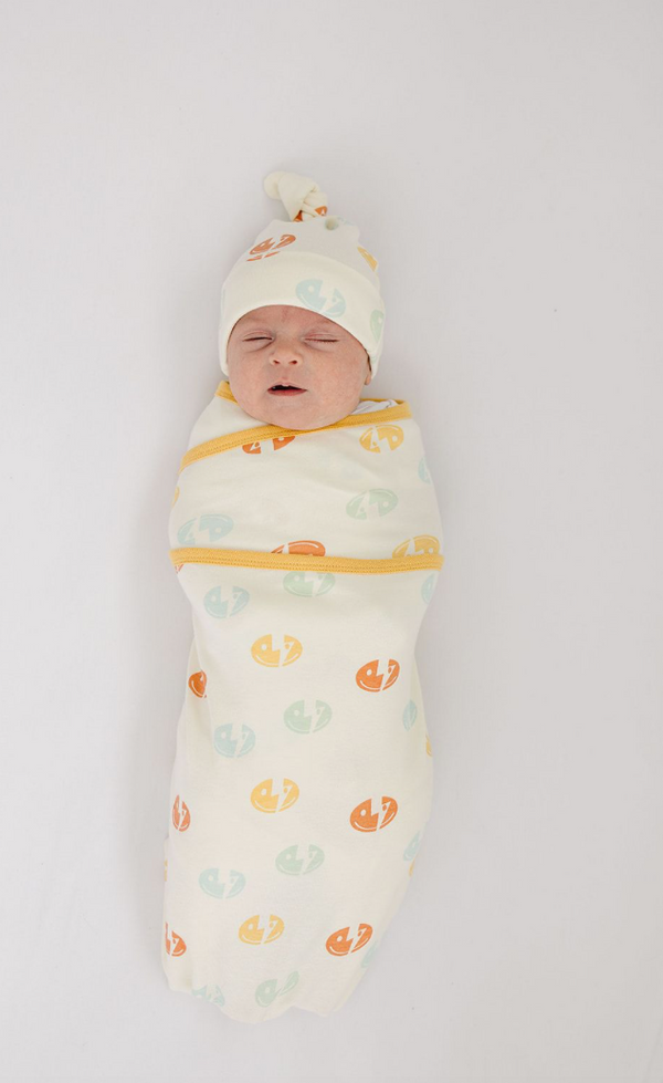 Sleeping newborn wearing a GOTS certified organic cotton knotted hat with smiley bolt print, wrapped in matching swaddle.