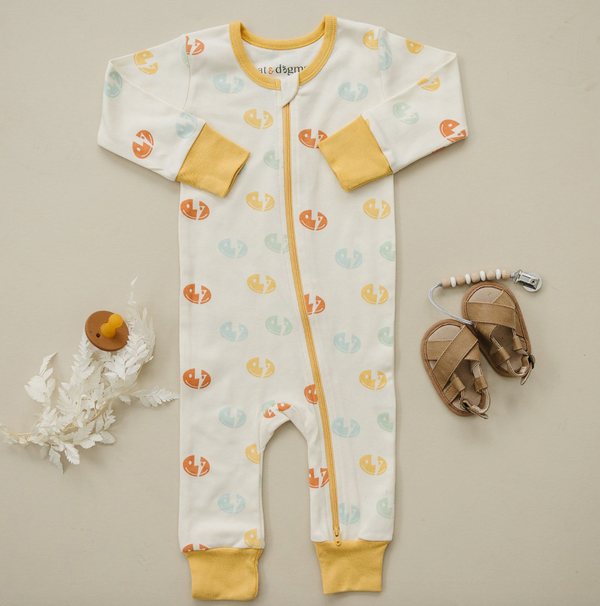 GOTS certified organic cotton baby romper with colorful smiley bolt print, yellow cuffs, front zipper, sandals, and wooden pacifier clip.