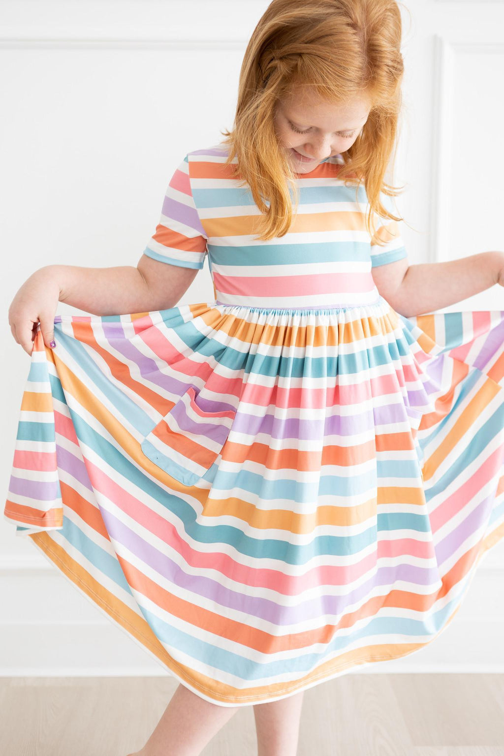 Girl smiling in a colorful Spring Stripes Short Sleeve Pocket Twirl Dress for Girls, showcasing the twirly skirt design perfect for playful moments. Ideal twirl dress for girls.
