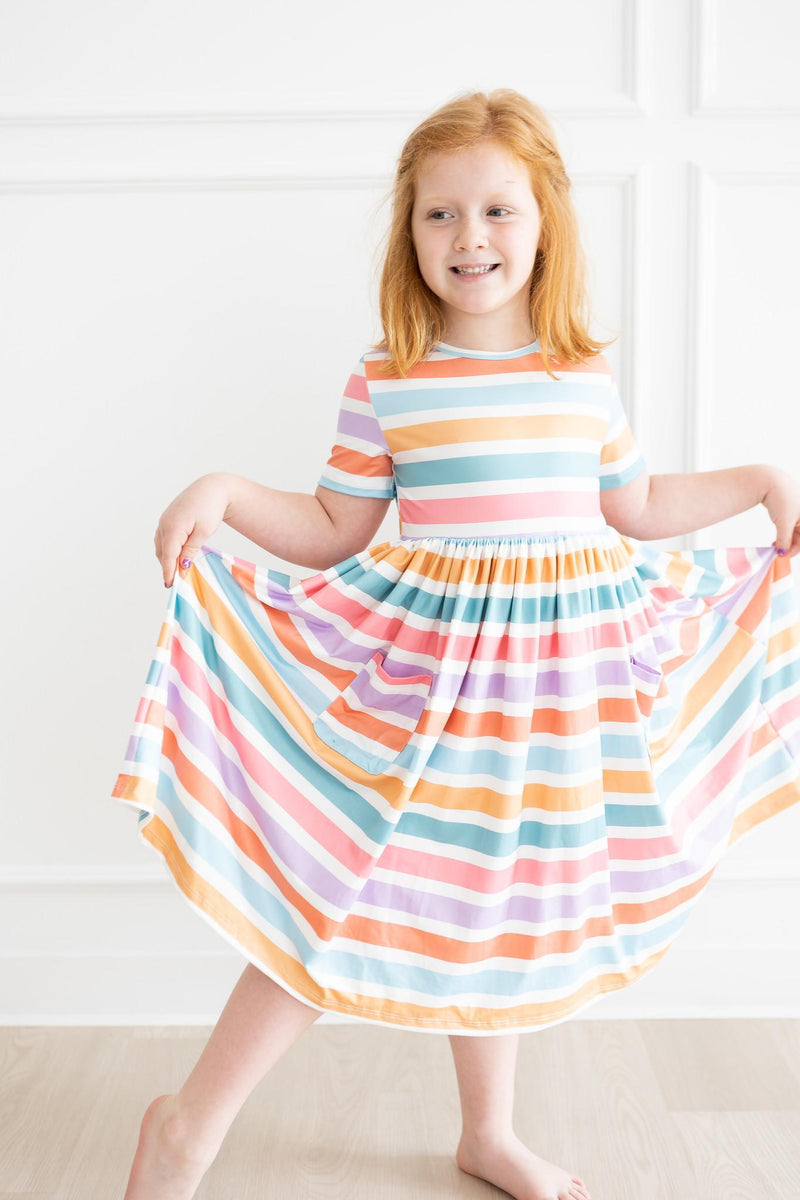 Girl delightfully twirling in a Spring Stripes Short Sleeve Pocket Twirl Dress for Girls, emphasizing the bright stripe pattern and comfort, a lovely twirl dress for girls.