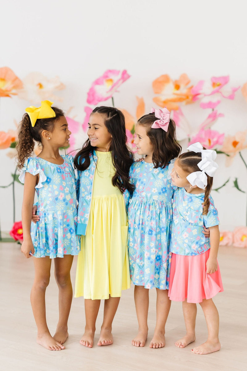 Four children happily wearing colorful outfits, including the Springtime Splendor Satin Jacket, surrounded by a backdrop of vibrant flowers, showcasing a fun and stylish look.