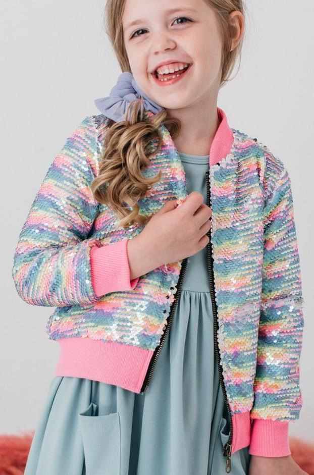 A young girl smiling and wearing the Sprinkles Flip Sequin Jacket from Mila & Rose, highlighting colorful sequins in a joyful setting.