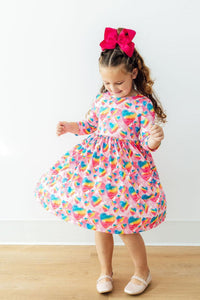 Sugar & Spice 3/4 Sleeve Pocket Twirl Dress with rainbow-heart print; girl twirls in pink dress and pink bow.